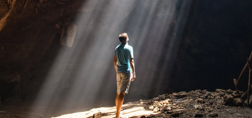 Ein Mann steht in einer Höhle und blickt zu einem Spalt in der Decke, durch den die Sonnenstrahlen fallen.