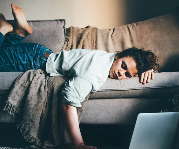 Frau liegt erschöpft auf einem Sofa, eine Hand am Laptop