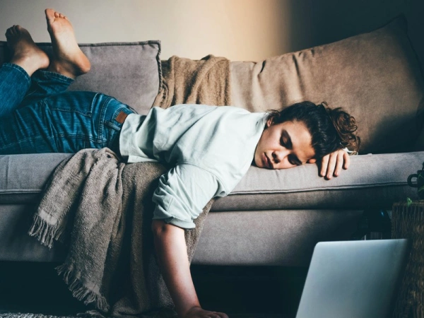 Frau liegt erschöpft auf einem Sofa, eine Hand am Laptop