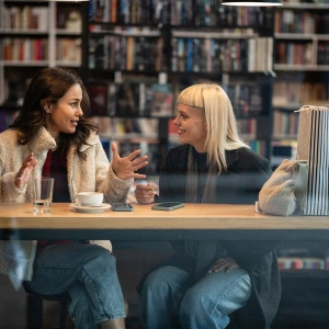 Junge Frauen mit Getränk in engagiertem Gespräch vor Bücherwand
