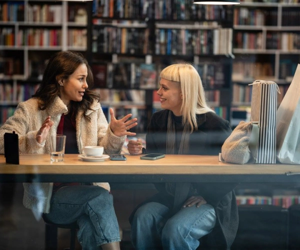 Junge Frauen mit Getränk in engagiertem Gespräch vor Bücherwand