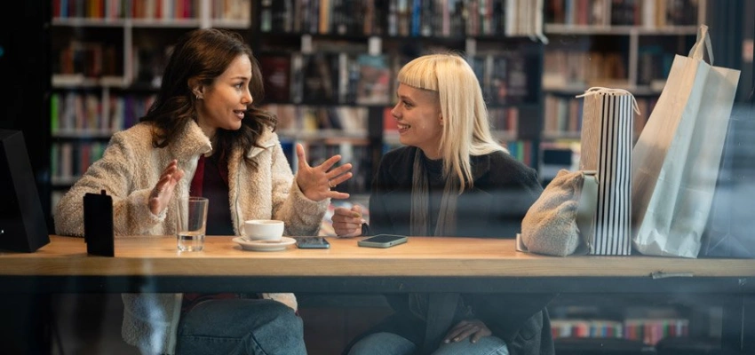 Junge Frauen mit Getränk in engagiertem Gespräch vor Bücherwand